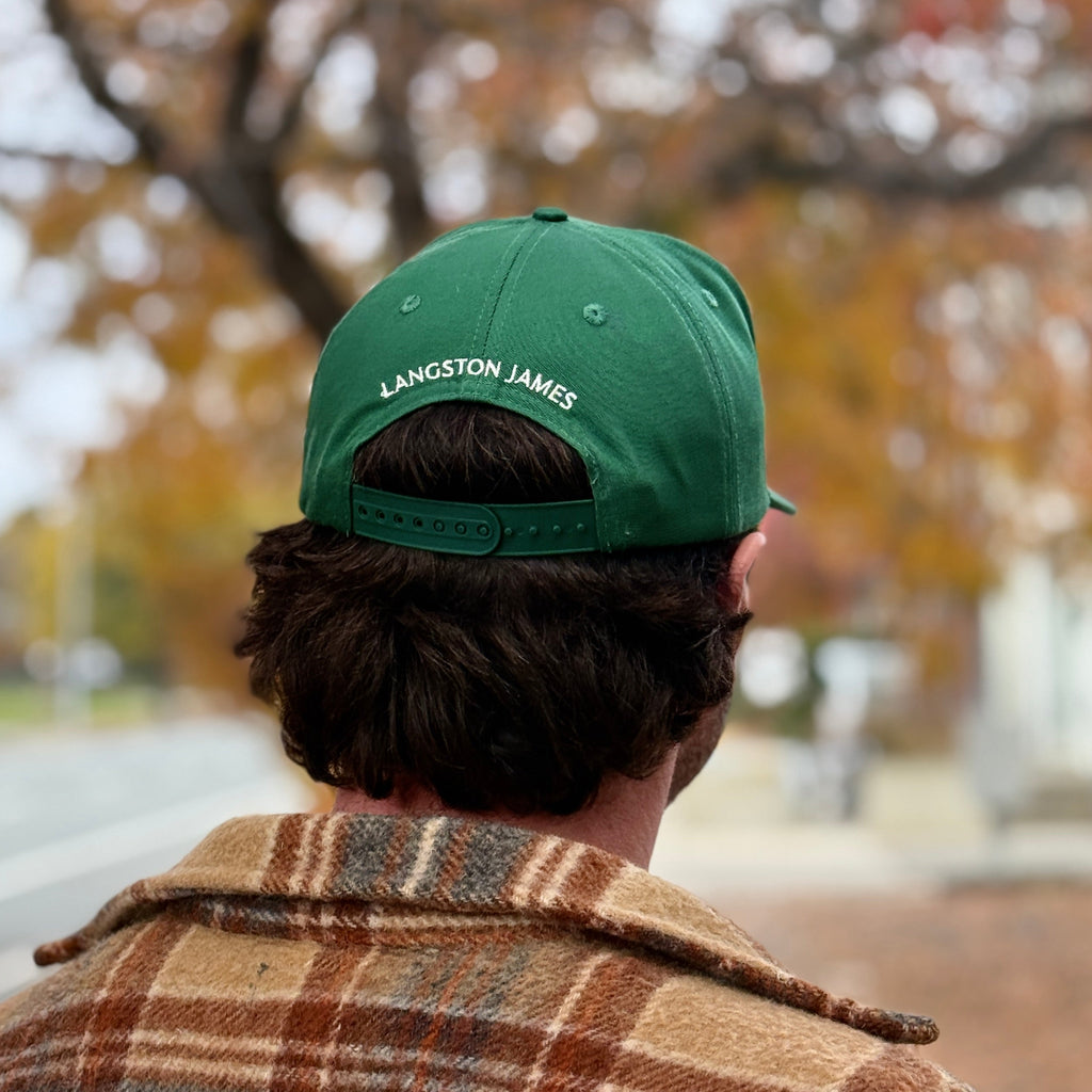 Person wearing a green cap with 'Langston James' logo, standing outdoors with trees in the background.